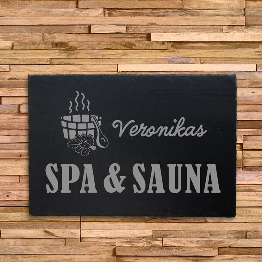 Dekoschild aus Schiefer mit dem Motiv SPA & SAUNA, welches auf eine Schieferplatte in der Größe 30 x 20 cm  und personalisierter Form mittels Laser graviert wird. Ergänzend zu dem Wunschnamen und dem Text SPA & SAUNA ist ein Saunazuber mit Saunakelle.