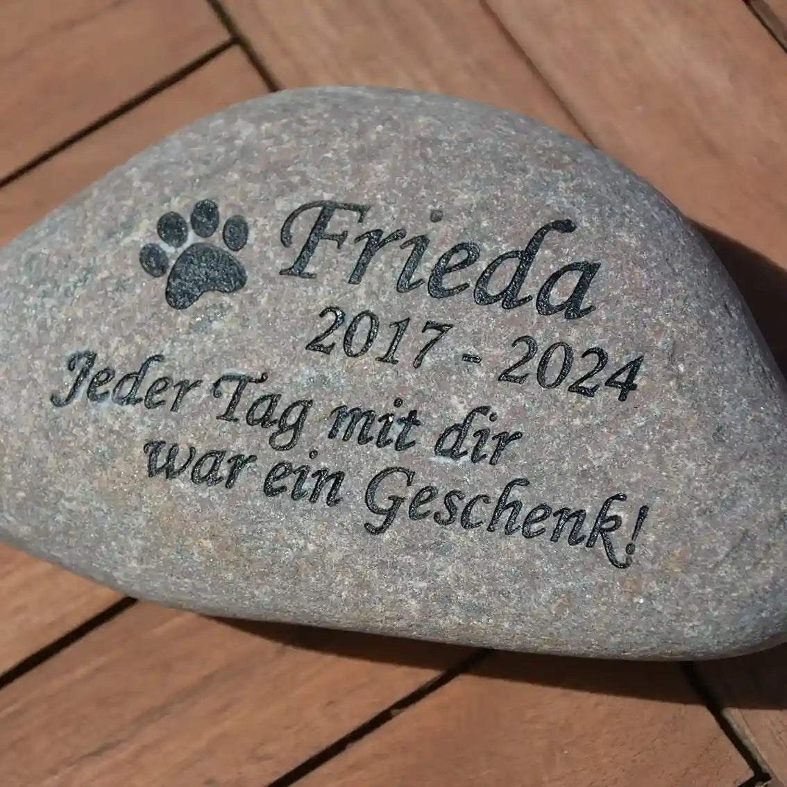 Musterbeispiel für einen Naturstein Findling als Tiergrab mit Namen des verstorbenen Hundes, Lebensdaten, Abschiedsworte und einer Pfote als Symbol mit eingefärbter schwarzer Gravur