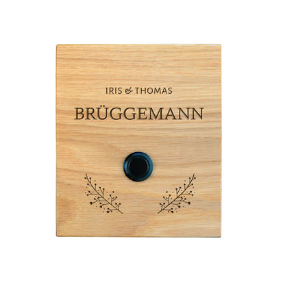 Klingelschild Motiv Brüggemann aus edler Eiche mit Tasterauswahl unbeleuchteter Taster, LED-Taster oder schwarz-Aluminium-Taster in der Größe 12 x 14 cm oder 14 x 25 cm. Name wird per Laser in das Holz graviert. Mit zwei grazilen Zweigen rechts und links unterhalb des Tasters und klassischer Schrift.