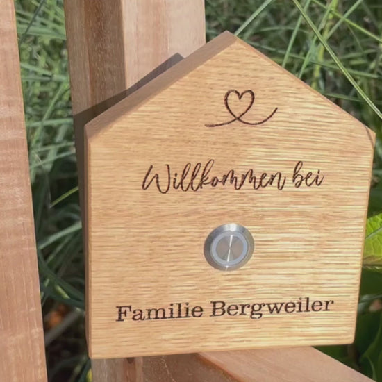 Klingelschild in geschnittener Hausform aus edler Eiche mit Auswahl eines unbeleuchteten Tasters, LED-Taster oder schwarz-Aluminium-Taster in der Größe 12 x 14 cm oder 14 x 25 cm. Name wird per Laser in das Holz graviert. Mit einem geschwungenem Herz in der Dachspitze und in geschwungener Schrift "Willkommen bei" und unterhalb des Tasters "Familie" und der Nachname