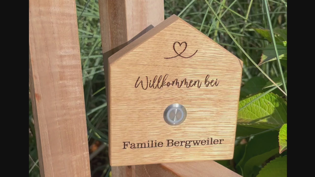 Klingelschild in geschnittener Hausform aus edler Eiche mit Auswahl eines unbeleuchteten Tasters, LED-Taster oder schwarz-Aluminium-Taster in der Größe 12 x 14 cm oder 14 x 25 cm. Name wird per Laser in das Holz graviert. Mit einem geschwungenem Herz in der Dachspitze und in geschwungener Schrift "Willkommen bei" und unterhalb des Tasters "Familie" und der Nachname