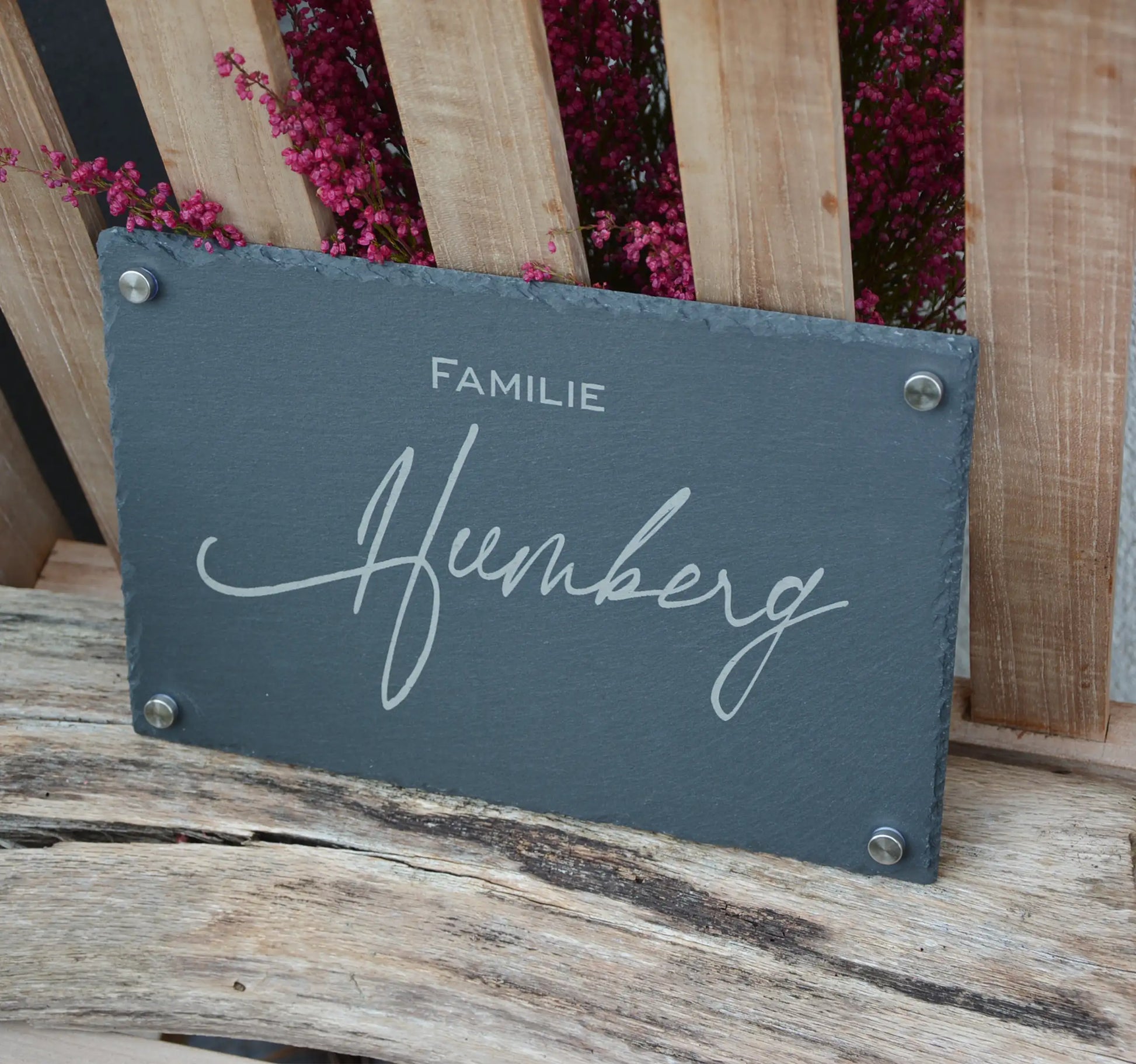 Tür- und Namensschild aus Schiefer mit schwungvoller Handschrift in personalisierter Form in der Größe 30 x 20 cm. Hier als Beispiel Nachname mit "Familie" in kleinerer Zeile oberhalb des Namens mit 4 Abstandshaltern in Edelstahl matt.